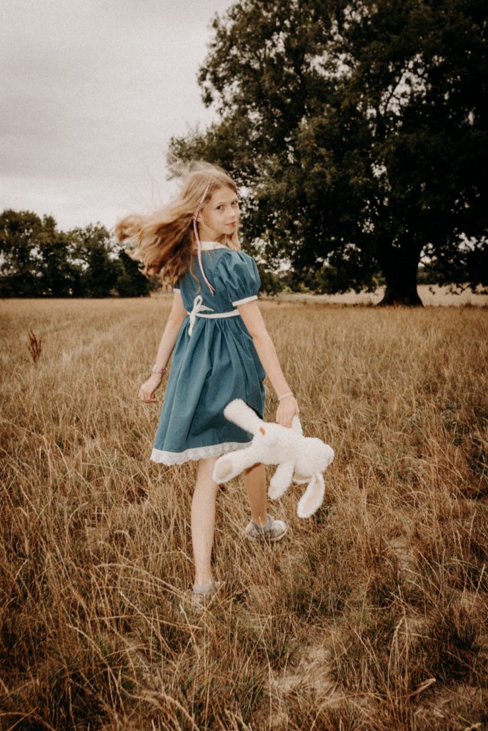 Petite fille dans un décor de forêt inspiré d’Alice au Pays des Merveilles, séance photo enfant